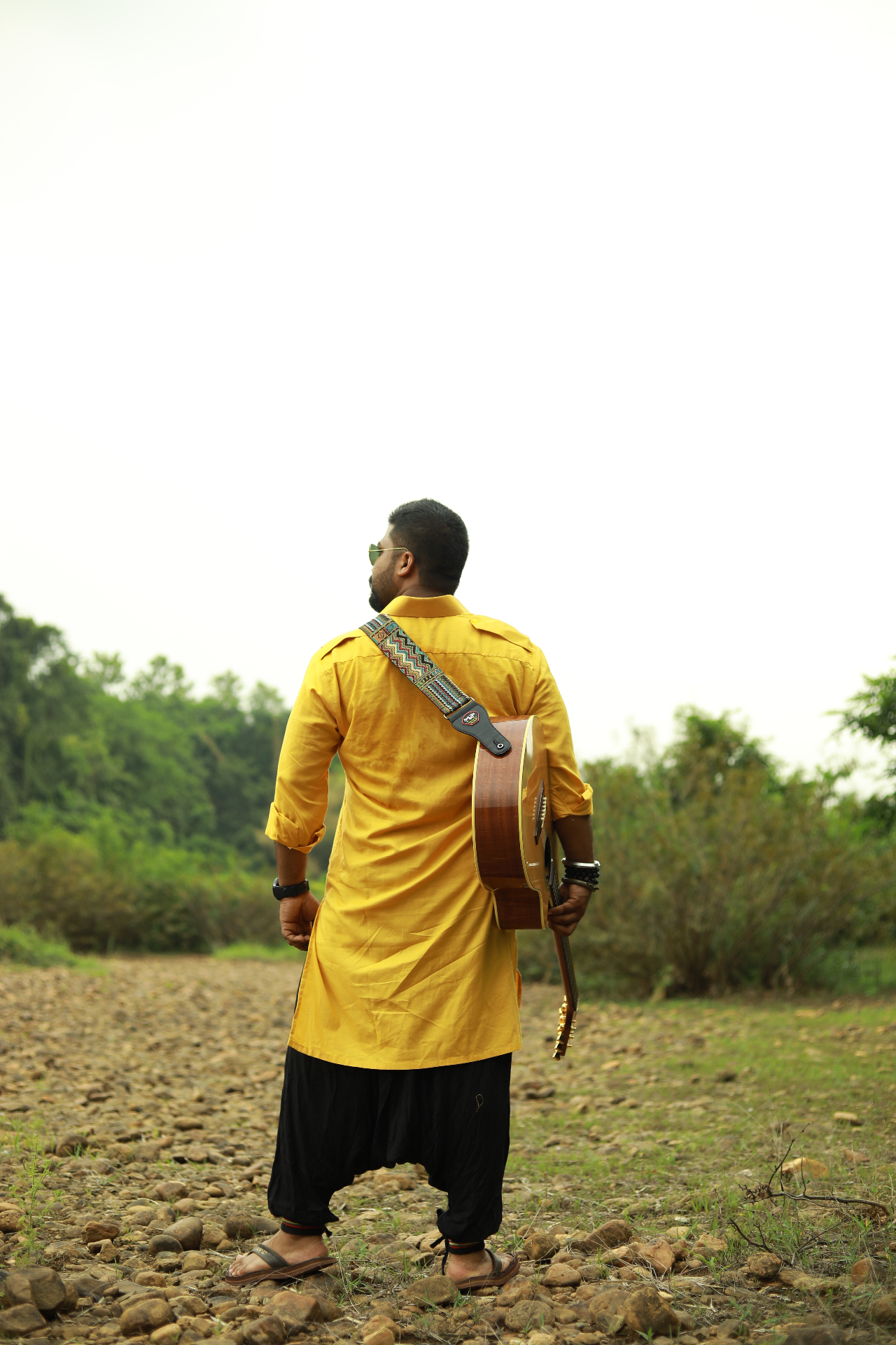 Shelin Chacko in mustard kurta with acoustic guitar in an open field